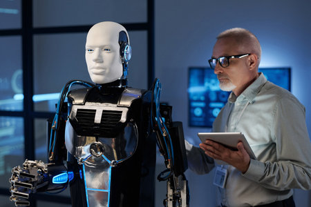 Mature engineer in eyeglasses using tablet pc to connect robotの写真素材