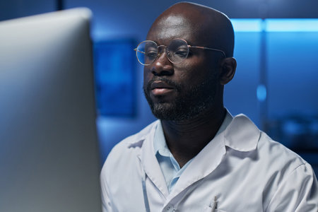 Serious African American engineer in eyeglasses using computer at his work in the laboratory