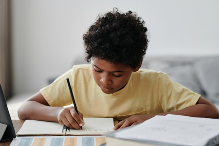 African American little boy doing homework at table at homeの写真素材