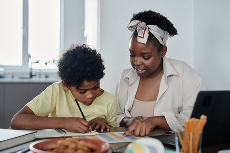 African American mom explaining material to her son while they sitting at table in the room, she...