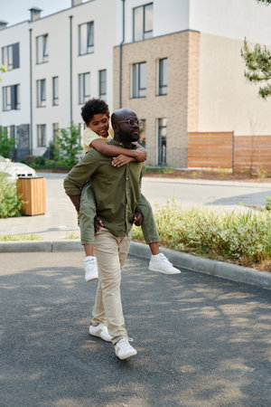 Vertical image of African American dad riding his son on his back during walk in the city