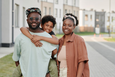 Portrait of African American family of three smiling at camera standing on the street in summer dayの写真素材