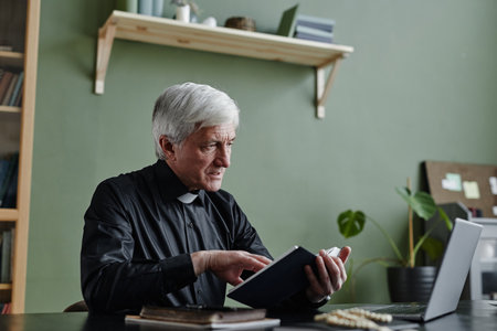 Side view portrait of white haired senior priest holding Bible while giving online religious support talk via video chat, copy spaceの写真素材