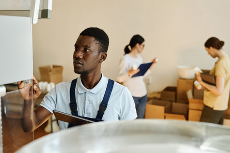 Waist up portrait of young black factory worker holding tablet while overseeing production, copy spaceの写真素材