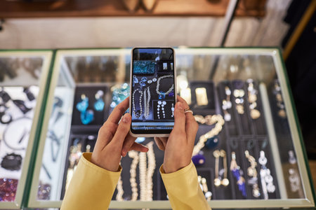 Top view closeup of unrecognizable young woman holding smartphone and taking photos or videos of jewelry display for social media, copy spaceの写真素材