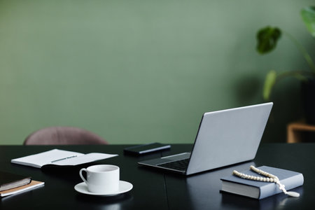 Minimal background image of office workplace desk with open laptop against green wall, copy space