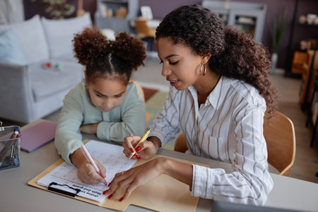 Portrait of black young woman explaining math to little girl in home education lessonの写真素材