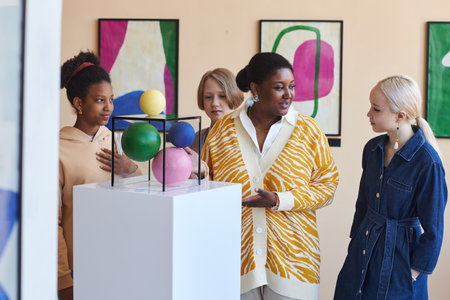 Diverse group of teenas listening to teacher or tour guide in modern art gallery