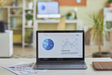 Background image of open laptop computer with statistics data charts on screen on office workplace,...