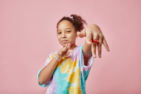 Pretty African American schoolgirl stretching one arm and keeping other bent in elbow while standing in front of camera and looking at youの写真素材