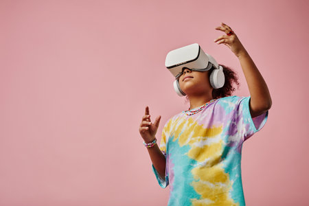 Cute girl in casualwear and VR headset standing in front of camera with copyspace on her right and playing virtual game in isolation in studioの写真素材