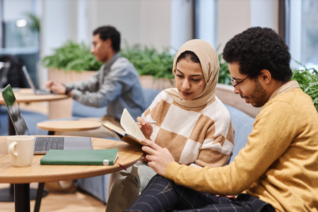 Portrait of modern Middle Eastern woman wearing head cover in office and looking at notes with male colleagueの写真素材