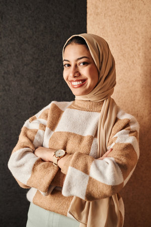 Minimal waist up portrait of smiling Arabian woman standing by two tone wall and looking at camera with confidenceの写真素材
