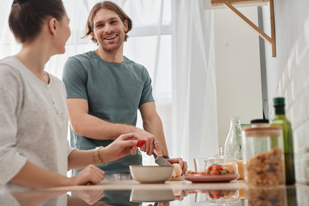 Side view portrait of happy couple making breakfast together in morning focus on young man smiling at girlfriend, copy spaceの写真素材