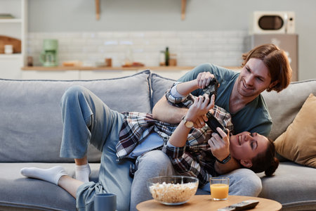 Portrait of playful young couple playing videogames on couch at home and holding controllers, copy spaceの写真素材