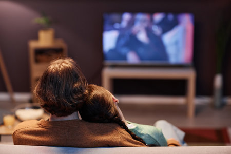 Back view of young couple watching TV together at home sitting on sofa in dark, copy spaceの写真素材