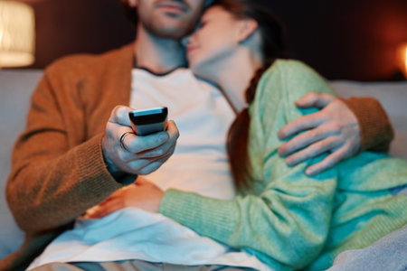 Closeup of young couple embracing affectionately watching TV together at home, copy spaceの写真素材