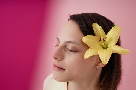 Closeup portrait of beautiful teenage girl with cerebral palsy and flower in hair against pink background, copy spaceの写真素材