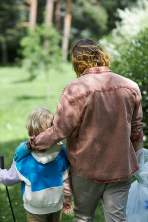 Back view of father and son embracing in park while picking up trash togetherの写真素材