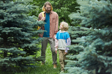 Full length portrait of modern father and son walking towards camera outdoors together exploring...
