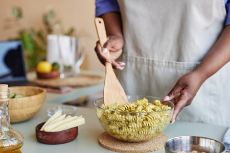 Close up of unrecognizable black woman mixing pasta in bowl while cooking in cozy kitchen, copy spaceの写真素材