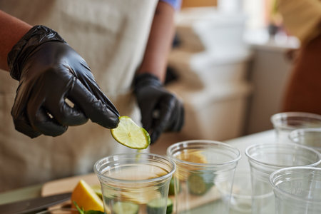 Close up of woman wearing glove adding lime slices to refreshing lemonade drinks in bar, copy spaceの写真素材
