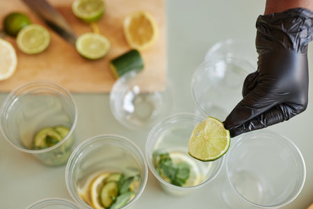 Top view closeup of young woman adding lime slices to drinks while making lemonade in bar, copy...