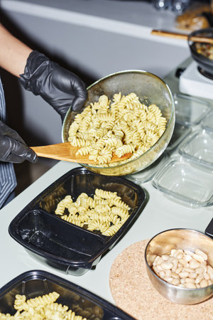 Vertical closeup of female hands putting pasta into plastic containers while working in food...