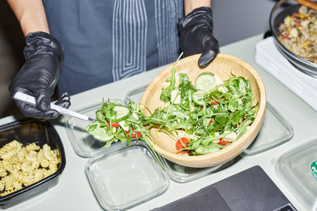 Closeup of female hands putting salad into plastic containers while working in food delivery, shot with flash, copy spaceの写真素材