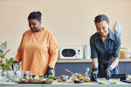 Portrait of two smiling African American women cooking together in kitchen and doing food prep at weekendの写真素材