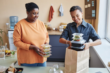 Waist up portrait of two African American women unpacking food delivery order at homeの写真素材