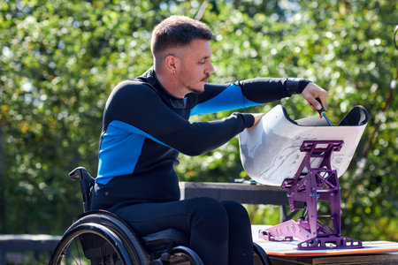 Side view portrait of man with disability assembling adaptive wakeboard equipment by lake and wearing scuba diving outfitの写真素材