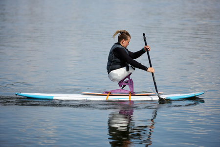 Side view portrait of young teenage boy with disability enjoying paddleboarding on lake with...