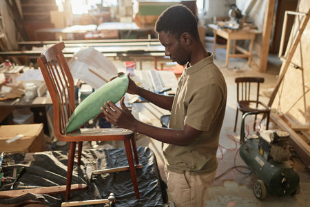 Side view portrait of young African American craftsman refurbishing vintage furniture in rustic workshop, copy spaceの写真素材