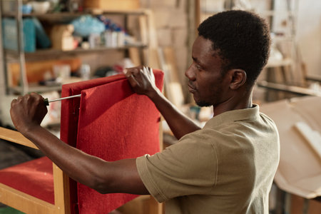 Side view portrait of young black man refurbishing old armchair in carpentry workshop, copy spaceの写真素材