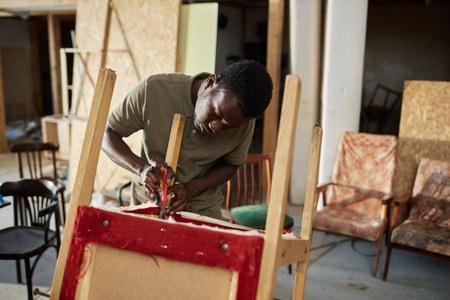 Waist up portrait of young black man repairing old furniture in carpentry workshop, copy spaceの写真素材