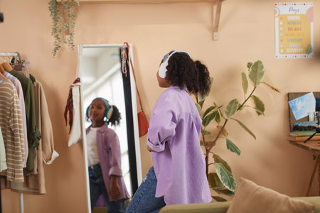 Back view of young black girl dancing by mirror wearing headphones at home, copy spaceの写真素材