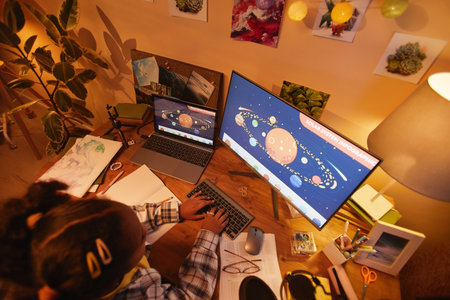 Top view at black girl using computer with space theme while studying at home in cozy evening light, copy spaceの写真素材