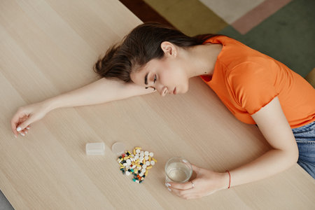 Top view of depressed young woman lying on table at home with pile of pills and tablets, copy spaceの写真素材