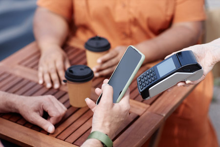 Closeup of unrecognizable person paying via NFC by smartphone at outdoor cafe, copy spaceの写真素材