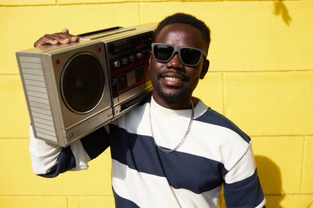 Vibrant waist up portrait of funky Black man holding boombox outdoors and smiling at camera