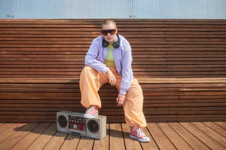 Full length fashion shot of bald young woman posing with boombox in urban city setting and wearing colorful trendy outfitの写真素材