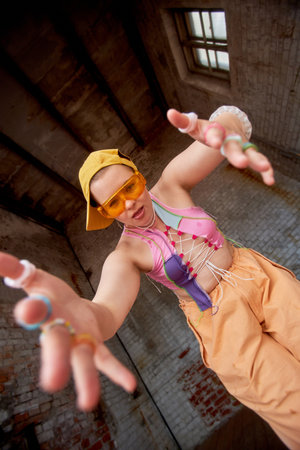 Colorful fashion portrait of tough young girl looking at camera dancing in urban setting low angle