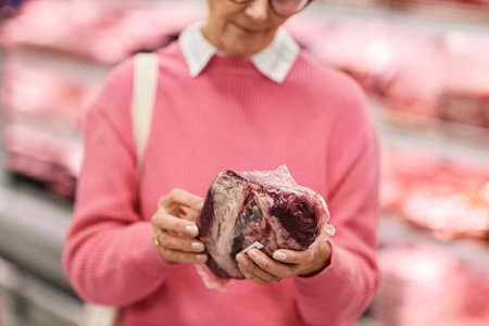 Close up of woman choosing fresh meat while shopping for groceries in supermarket, copy spaceの写真素材