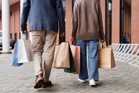 Back view of adult couple with shopping bags walking together outdoors by mall, copy spaceの写真素材