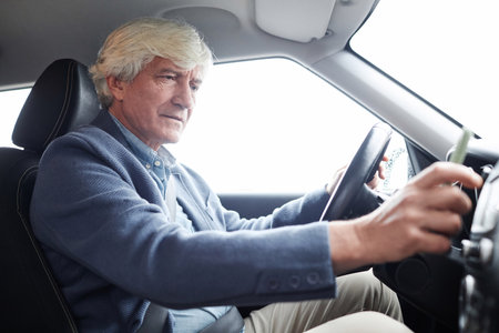 Side view portrait of white haired senior man using radio while driving in car, copy spaceの写真素材