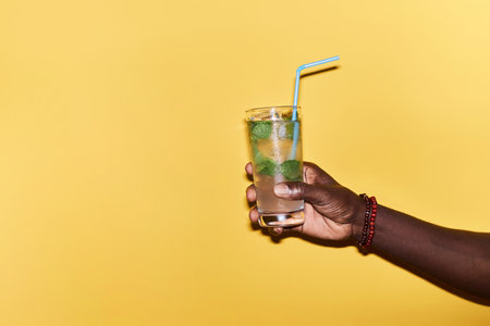 Minimal close up of male hand holding refreshing ice cocktail against vibrant yellow background, copy spaceの写真素材