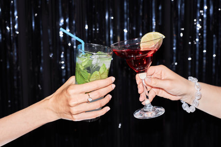 Close up of two people holding cocktail glasses against glittering party background, copy spaceの写真素材