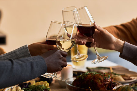 Close up of group of people toasting with wine glasses in celebration at Thanksgiving dinner table,...