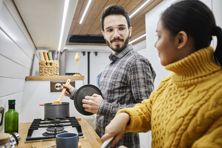 Side view portrait of young couple cooking together in trailer van while travelling togetherの写真素材